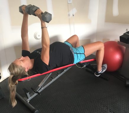 Home Advantage Pregnant woman exercising with dumbbells on a workout bench and a stability ball.