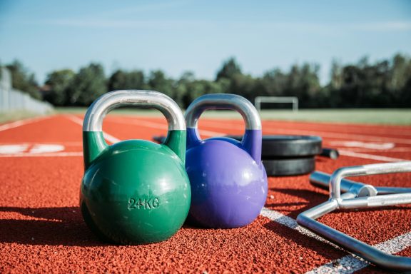 Functional Power A green and a purple kettlebell on a running track with exercise equipment in the background.