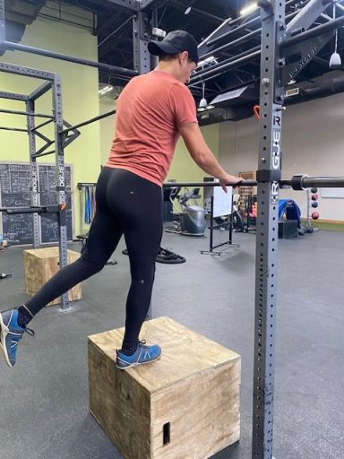 Max Muscle Burn A person in workout gear balanced on a wooden box, preparing to exercise with a barbell.